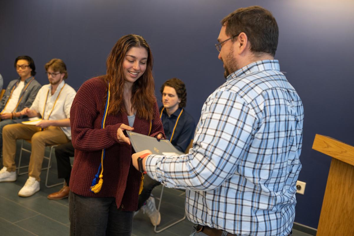 A student smiling as they receive recognition from the Economics Department for excellence in the major.