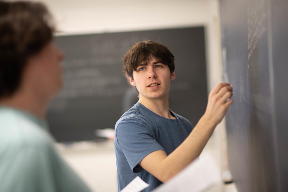 Student solving math equations on a chalkboard in a classroom.