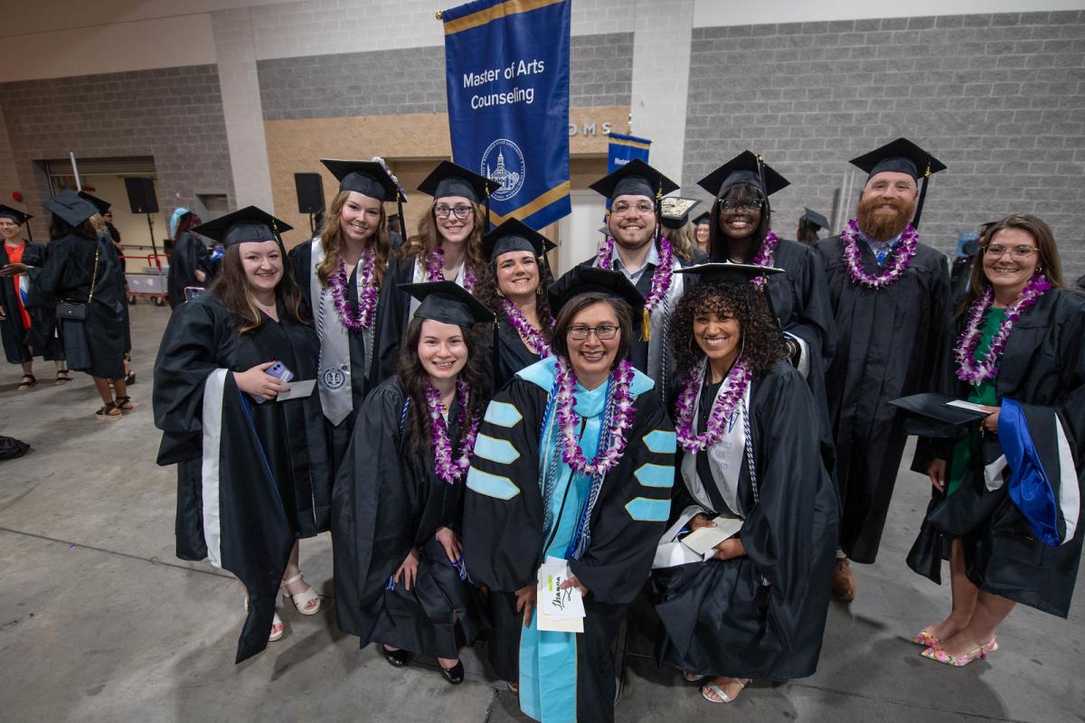 Counseling students smiling with a faculty member at graduate commencement.