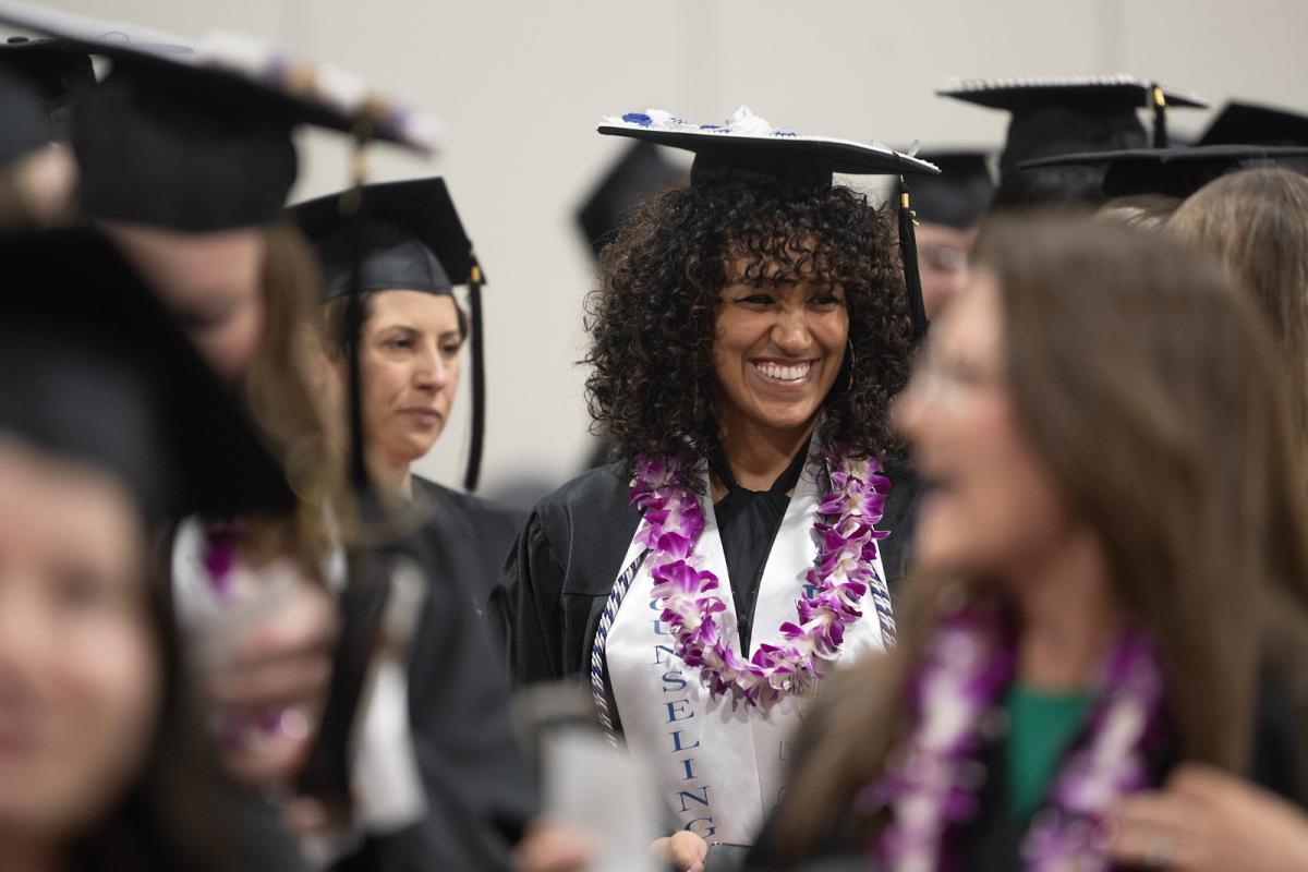 Counseling student smiling in cap and gown at graduate commencement ceremony.