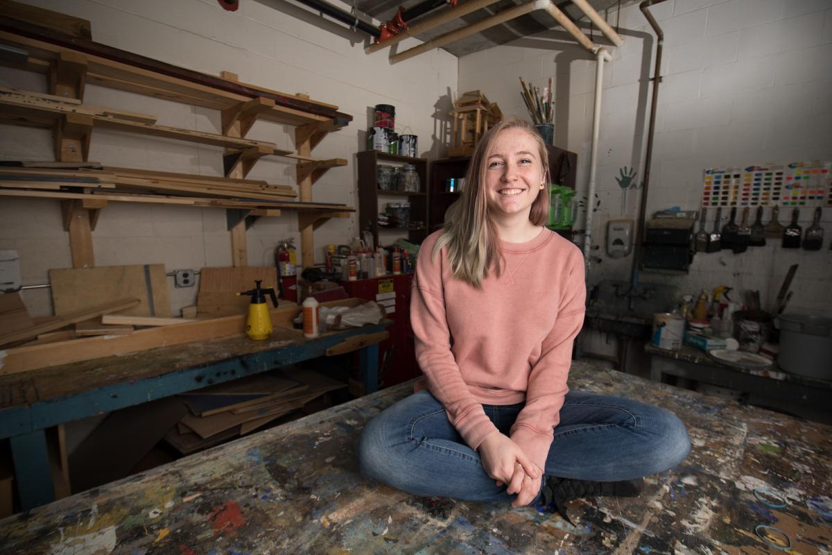 Theatre design major seated on a stage set smiling.