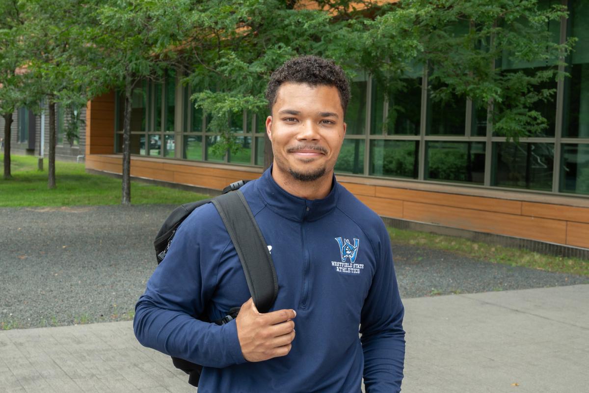 Student smiling outside on campus holding a backpack.