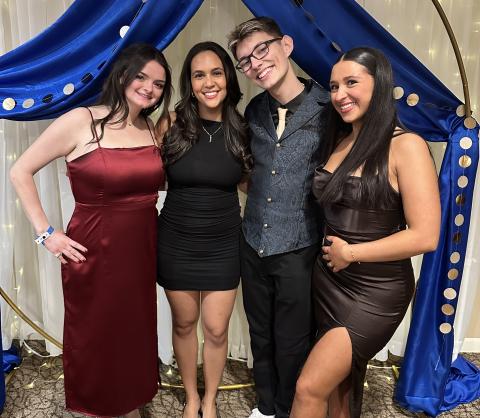 Group of students stand in front of formal backdrop