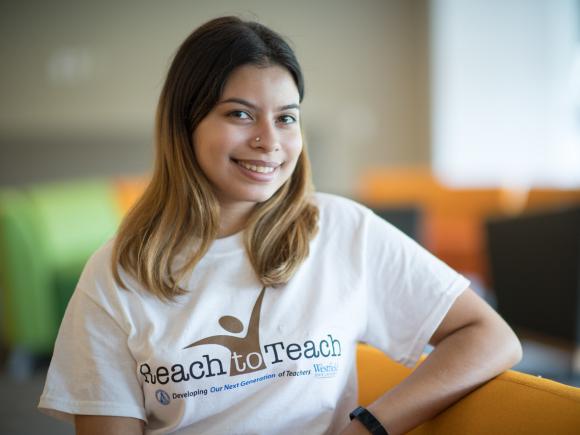 Reach to Teach student with long brown hair and nose ring wearing RTT shirt smiling.