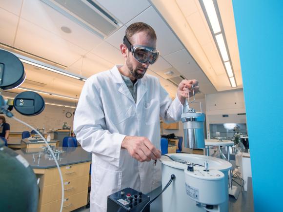 Individual in chemistry lab doing an experiment with eye protection and white gown.