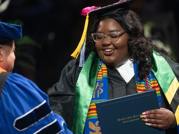 TRIO student at commencement holding a diploma.