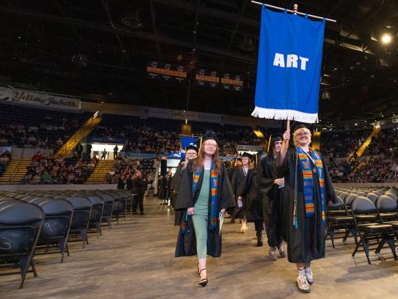 Art students at undergraduate commencement ceremony holding art banner.