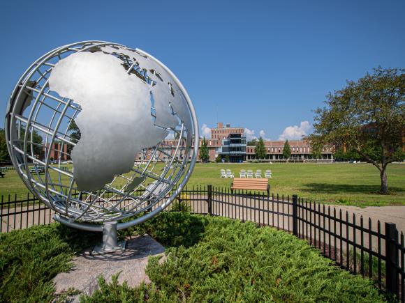 Campus globe in the summer in front of Ely Hall with blue skies.