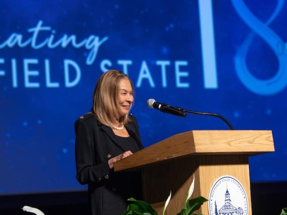 President Linda Thompson of Westfield State giving a keynote speech in front of a blue screen that says "Celebrating 185 Years of Westfield State".