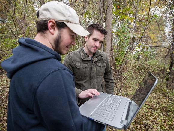 Two students conducting fieldwork for a class, examining data on a laptop outdoors.