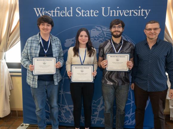 Three computer science students smiling alongside a faculty member at the Academic Excellence Awards ceremony.