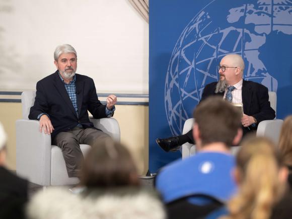 Two men sit on a stage talking to an audience