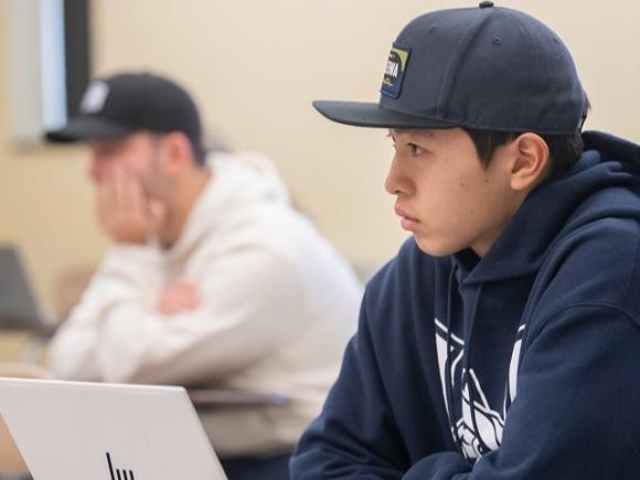 Management student in a classroom, listening attentively to an instructor.