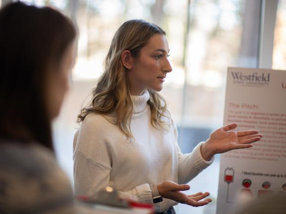 Student presenting a business pitch during a campus Shark Tank-style event.