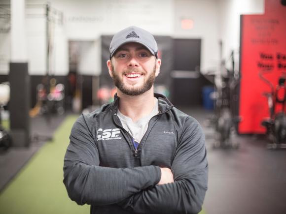 Student smiling in a campus gym with fitness equipment in the background.