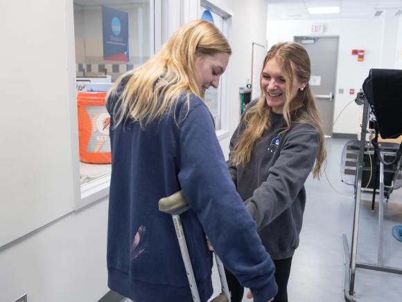 Movement science students in a lab fitting a classmate with crutches.