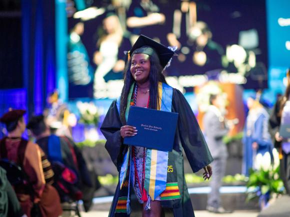 Graduate walks from stage holding diploma