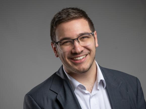 Smiling student intern in a suit jacket against a plain gray background.