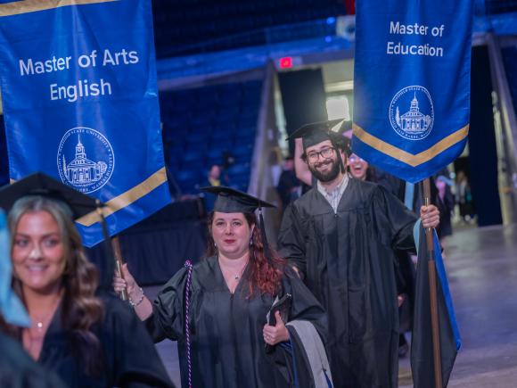 English graduate student holding M.A. English flag at commencement.