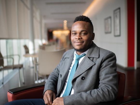 MPA student in a coat and tie smiling inside a campus building.