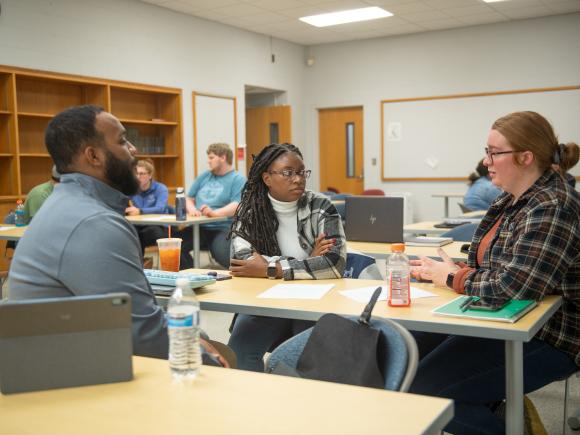 Three MPA students in a classroom actively engaged in a small group discussion.
