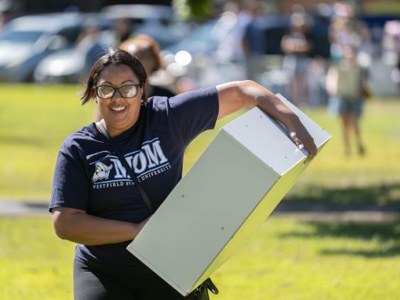 Woman wearing a tshirt that says Westfield State Mom carries a heavy item