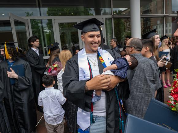 Student holding a child at undergraduate commencement smiling.