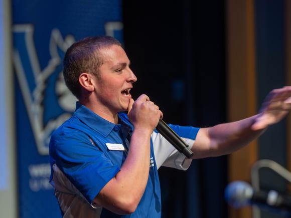 Matt Crusha ’27 speaks into a microphone and welcomes students during a Westfield State orientation event.