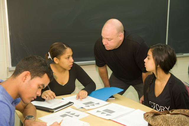 Math professor working with a small group of three students who are working on a math assignment.
