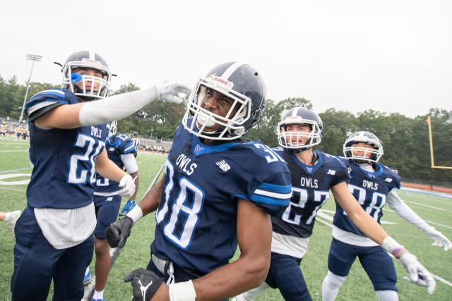 WSU football ream wearing blue jerseys with "Owls" written on them. Group of four students at game in uniforms.