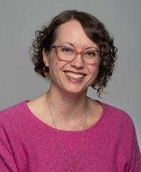 Charlotte wearing pink shirt with glasses and short brown hair smiling.