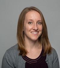 Kaitlin wearing black and gray shirt smiling with shoulder length hair.