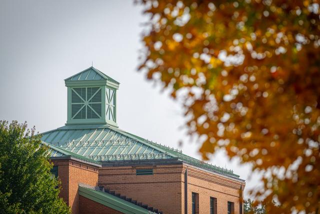 Courtney Hall in the fall with a tree in front of it with orange leaves.