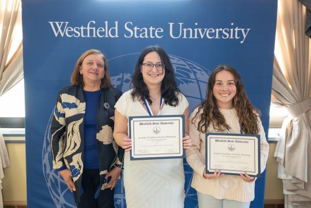 Faculty member smiling with two students during an academic awards ceremony.