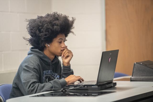 Computer science student working on a classroom project, focused on their laptop.