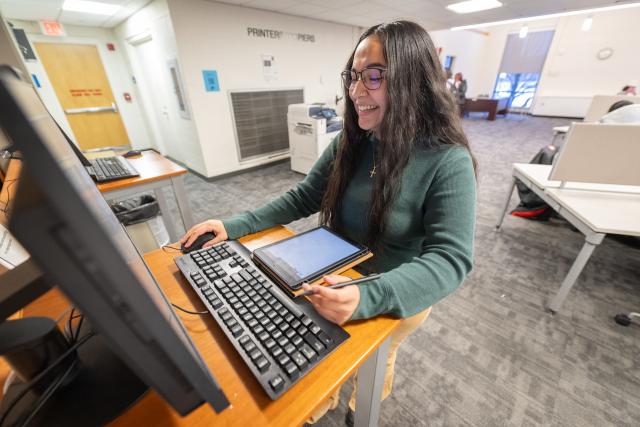 Student smiling while working on an assignment at a computer station in the campus library.