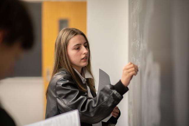 Student solving equations on a chalkboard in a math classroom.