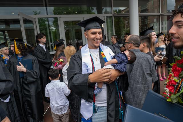 Student holding a child at undergraduate commencement smiling.
