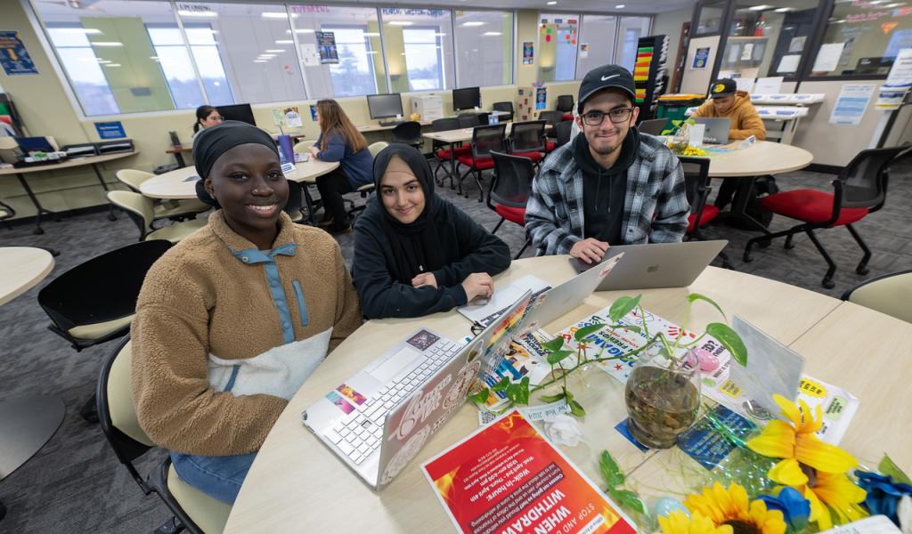Three students in the CARE Center smiling at round table.