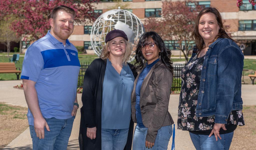 SAIL staff group photo with four staff members smiling in front of the campus globe.