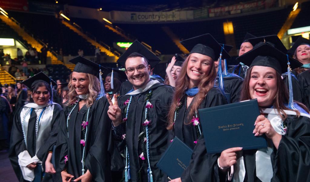 Students at commencement smiling wearing caps and gowns.
