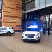 Two police vehicles are parked in front of University Hall, with a small crowd of people loading supplies for the Stuff-a-Cruiser event.