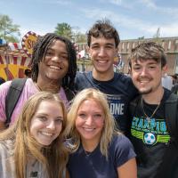 A group of five ,ale and female Westfield State students smile at the camera during the FlightFest carnival on the campus green