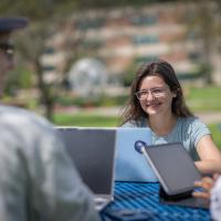 Three students sitting outside on a sunny day, working on laptops.