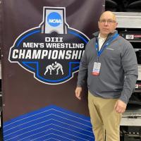 Paul Higgins stands next to banner for NCAA DIII Wrestling Championship