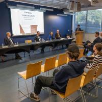Legal professionals participate in Westfield State University's Pursuing a Career in Law forum as students listen from the audience and a moderator stands at the podium